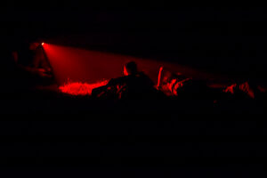 Two people lie on the ground in darkness, illuminated by a narrow red beam of light from a flashlight—a scene evoking the discipline and resilience instilled at Valley Forge Military College, where every cadet learns leadership even in the shadows.
