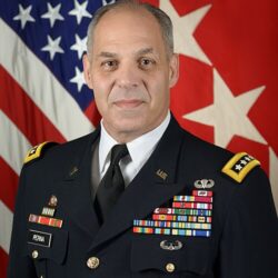 A U.S. Army general and Valley Forge Military College graduate poses in uniform before an American flag and a red flag with white stars, showcasing medals, badges, and a name tag reading PERNA—symbolizing his lifelong commitment to leadership.