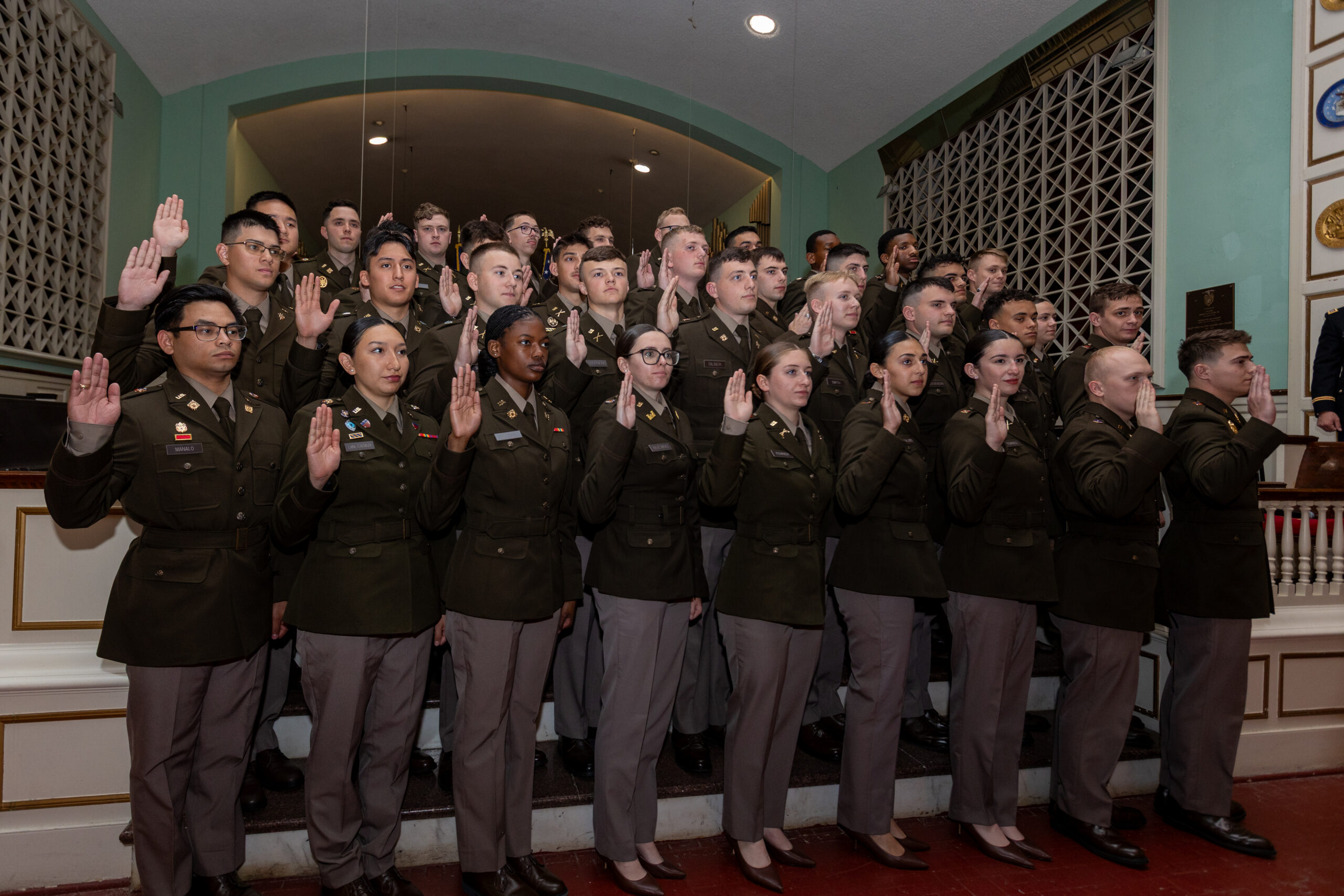 A group of uniformed individuals stands with their right hands raised, appearing to take an oath together in a formal indoor setting with ornate decor.