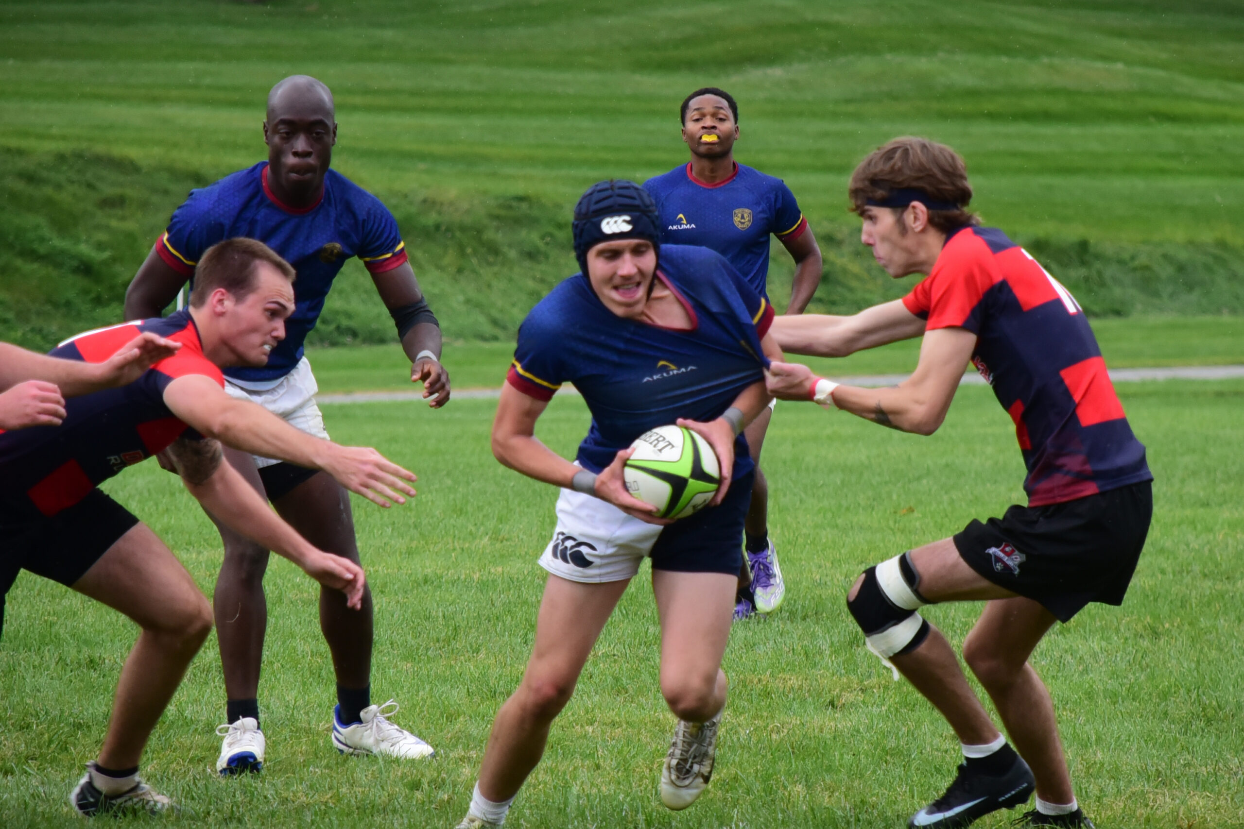 Rugby players in team uniforms competing for the ball on a grassy field.